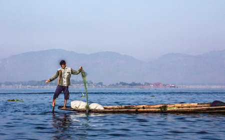 A fisherman at Inle lake is catching fish with a net . In the background are the mountains.のeditorial素材