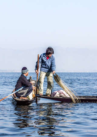 A fisherman at Inle lake is catching fish with a net . In the background are the mountains.のeditorial素材