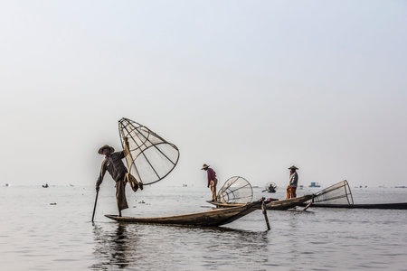 A fisherman at lake Inle, Myanmar holds up his fish trap. in the background are more fishermen.のeditorial素材