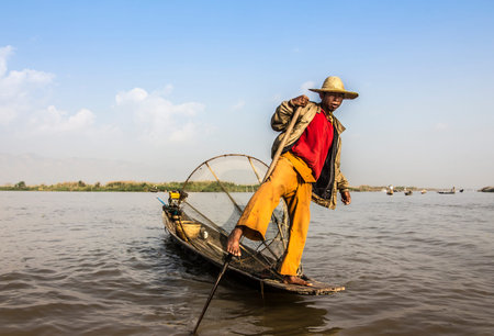 A fisherman at lake Inle, Myanmar stands in his boat, his fish trap is behind him.