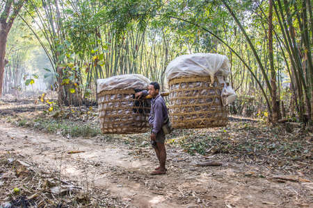 A man is carrying a big load in two baskets on his shoulder. he comes from a market at the bank of lake Inle, Myanmar.のeditorial素材