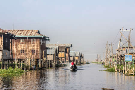 A boat is speeding through the "main road" of a stilt village at the Inle lake, Myanmar.のeditorial素材