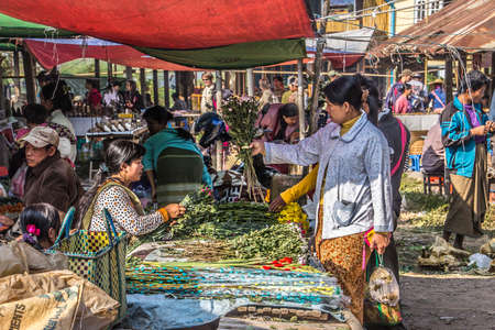 A market vendor at a market at the bank of the famous lake Inle, Myanmar. She is selling flowers to a customer.のeditorial素材