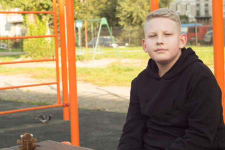 the young man in theme jacket with blond hair is sitting on the Playgroundの写真素材