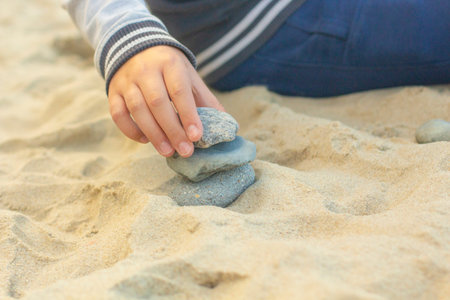 children's hand builds a tower of stones on the yellow sand