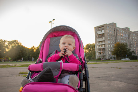 a little girl with blond hair sitting in a red stroller