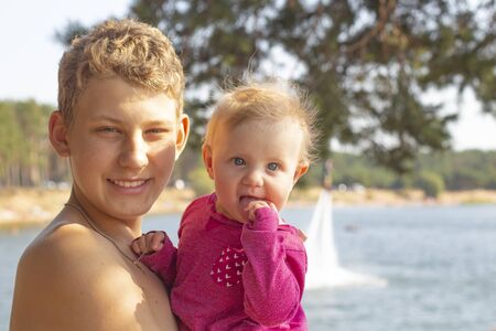 a teenager with blond hair holds a little girl in his arms.close upの写真素材