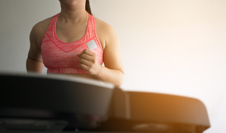 Woman in sportswear running on treadmill while training in gymの写真素材