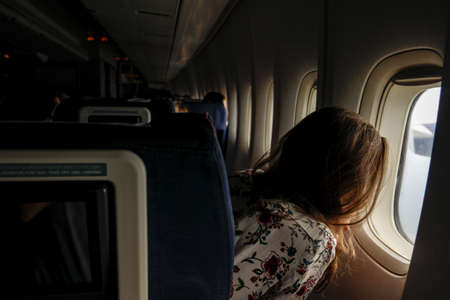 The girl is looking in the porthole in a planeの写真素材