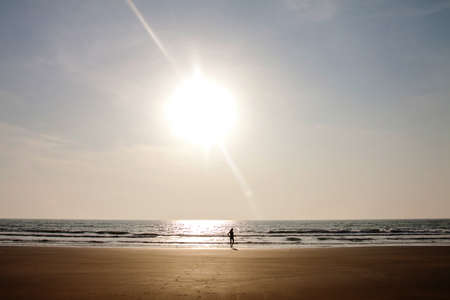 girl walking towards the ocean on a sand shoreの写真素材