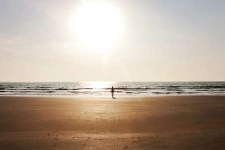 girl walking towards the ocean on a sand shoreの写真素材