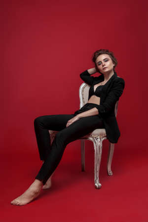 portrait of young girl in black suit on red background sitting poseの写真素材
