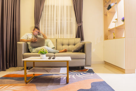 Man using tablet computer while sitting on sofa in living room at homeの写真素材