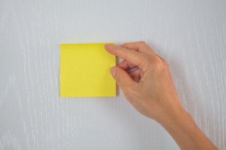 Hand holding yellow sticky note on the white wood wall background, stock photoの写真素材