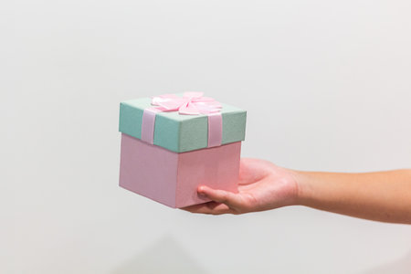Hand holding a gift box with pink ribbon and bow on white backgroundの写真素材