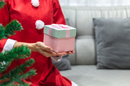 Woman in santa claus costume holding christmas gift box at homeの写真素材
