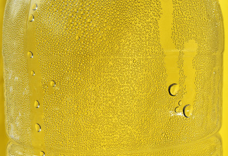 Many water drops on the surface of a transparent plastic bottle on yellow background, Abstract...