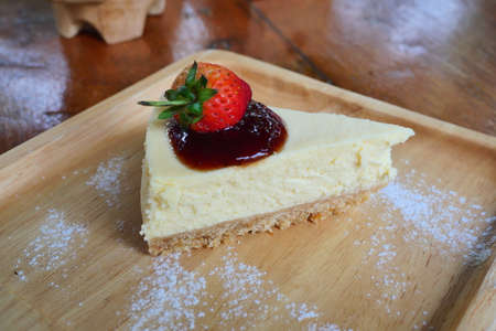 Cheesecake pie slice topped with strawberry syrup on a wooden plate, Sweet food with brown table in backgroundの写真素材