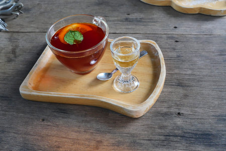 Hot lemon tea with mint leaf in a transparent glass and honey on a wooden tray, Brown beverage on a...