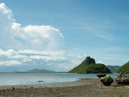 Mountain and green forest on the island and reef boulders on sandy area, Beach with sea smooth and Cumulus cloud on beautiful blue sky at Prachuap Bay, Prachuap Khiri Khan, Thailandの写真素材