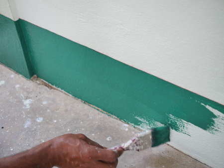 Painter painting green color acrylic on house concrete wall with a paintbrush, The sunburned hand of...