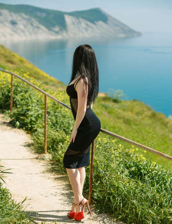 an attractive girl walks through colored meadows against the background of the sea and mountains.の写真素材