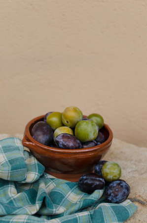 Vertical artistic still life with ceramic bowl full of fresh juicy green and black plums just picked from the tree. Fruit harvest, ecological agriculture concept. Out of focus background. Copy spaceの写真素材