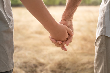 Unrecognizable grandfather and grandson holding hands walking in nature. Care, assistance, trust concepts. Bonding with family in retirement. Very close-up horizontal photograph with copy spaceの写真素材