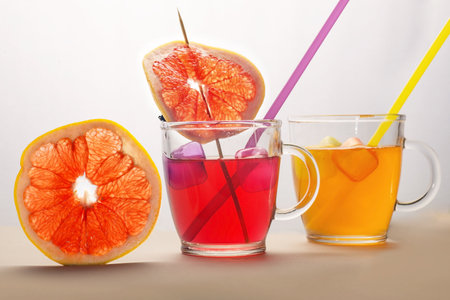 round slice slice of juicy grapefruit with two glass cups with yellow and red drinks with strawsの写真素材