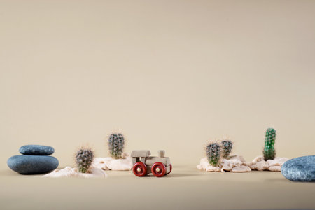 background image of wooden toy steam locomotive in desert with stones and cactuses on beige backdropの写真素材