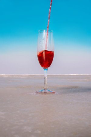 A stream of red wine is poured into a transparent glass against a blue sky on a sea coastの写真素材