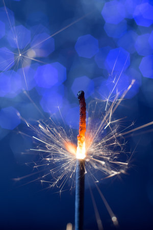 burning flickering sparkler new year fire on the background of blue lights bokehの写真素材