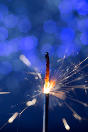 burning flickering sparkler new year fire on the background of blue lights bokehの写真素材