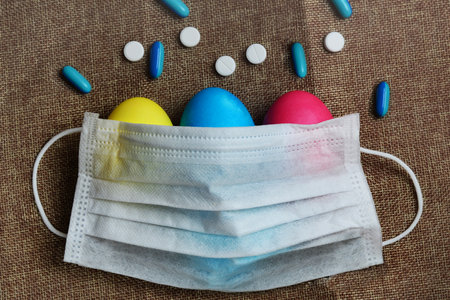 Colorful Easter eggs and medical mask on a burlap background.の写真素材