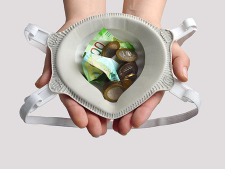 A child's hand holds a protective mask with money inside. The concept of protection against viruses and pollution.の写真素材