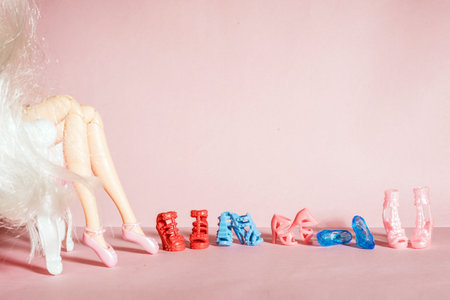 Doll legs on pink background and a row of toy shoesの写真素材