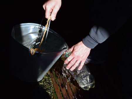 Hands of a man pouring water from a bucket on a black backgroundの写真素材