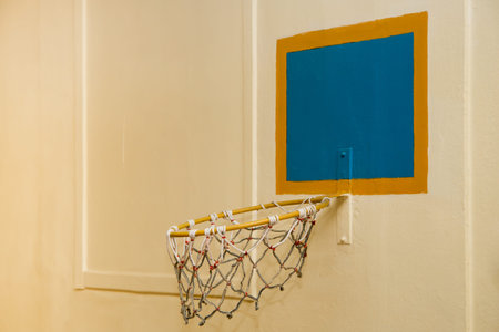 An old basketball hoop against a yellow wall. The basketball basket sagged down. The back is a blue...