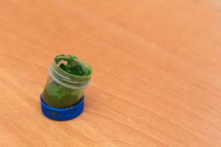 An old open jar of green gouache for painting. Side view of a half-empty can of gouache paint. There...