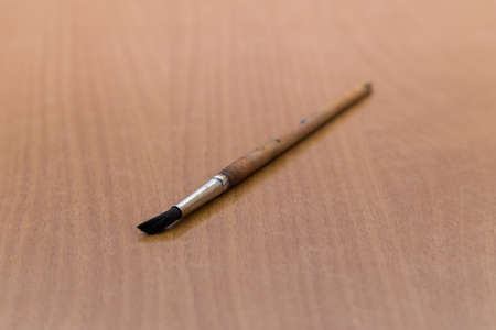 An artistic brush with a wooden handle lies on the table, one close-up. A tool for painting with paints on the artists desk. There is copy space. Warm soft daylight.の写真素材