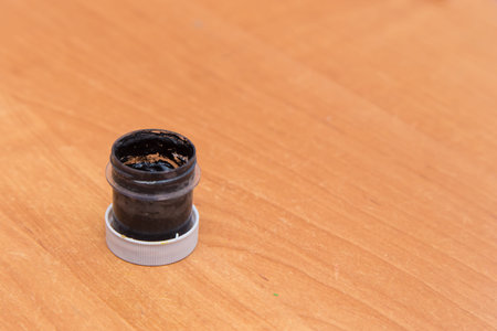An old open jar of black gouache for painting. Side view of a half-empty can of gouache paint. There...