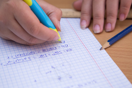 Close-up pupils hand solves a geometric problem in a notebook. A schoolboy performs a task at the...