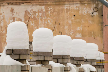Beautiful columns of snow on brick pillars. An even row of small snowdrifts against the background of a shabby wall. Urban winter landscape. Cloudy winter day, soft light.の写真素材