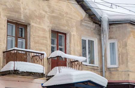 Sharp ice icicles hang from the drainpipe at the edge of the roof. Against the background of the wall of an old brick house. Large cascades, even beautiful rows. Cloudy winter day, soft light.の写真素材
