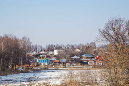 A small frozen river, rural houses in the background. Spring, snow melts, puddles and dry grass all around. Day, cloudy weather, soft warm light.の写真素材