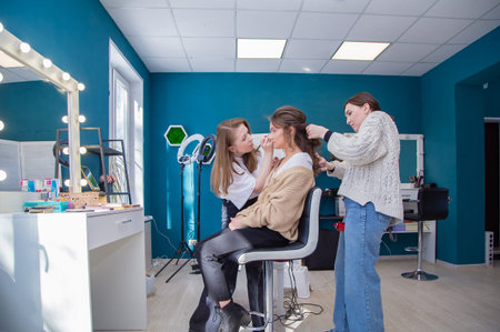 Two masters diligently do makeup and hair for a girl in the salon. Make-up artist and hairdresser...