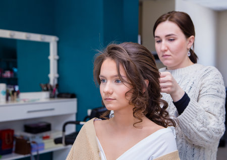 The face of a client girl, behind the master is styling her hair. The hairdresser makes a hairstyle for a young woman. Barber shop, business concept. Beauty salon, hair care.の写真素材