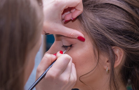 Close-up of the makeup artists hands draw arrows on the eyes with a brush. Female master makes makeup to a young woman. Business concept - beauty salon, facial skin care, cosmetology.の写真素材