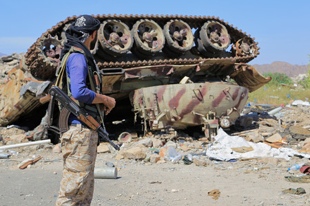 Yemeni soldier stands in front of one of the Houthi militia tanks after being destroyed by coalition aircraft west of the city of Taiz.のeditorial素材