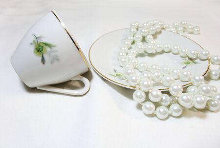 White cup and and saucer with drawings and white beads in saucerの写真素材